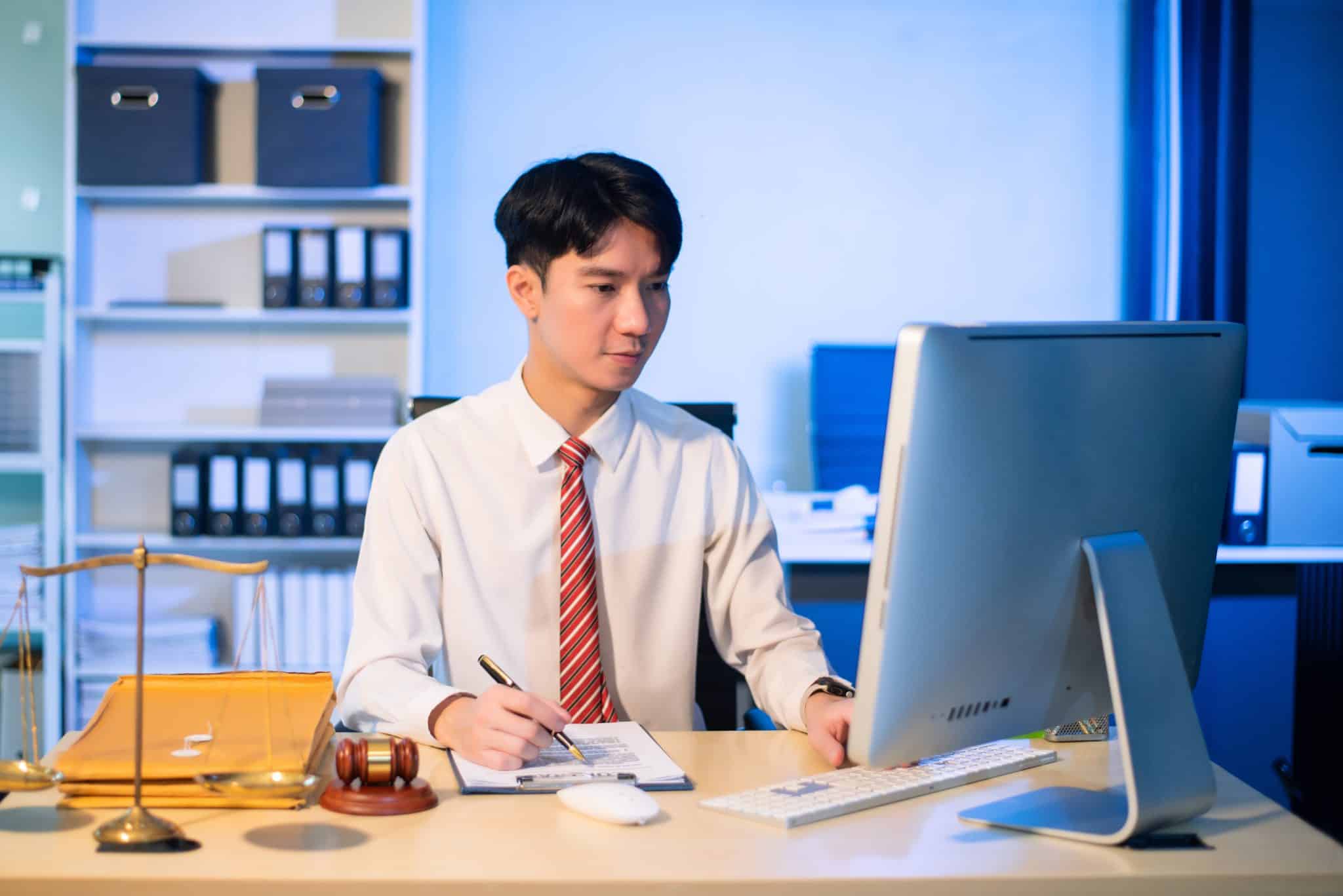 Yougn lawyer at desk with legal scales and gavel, writing documents in office, offering legal services